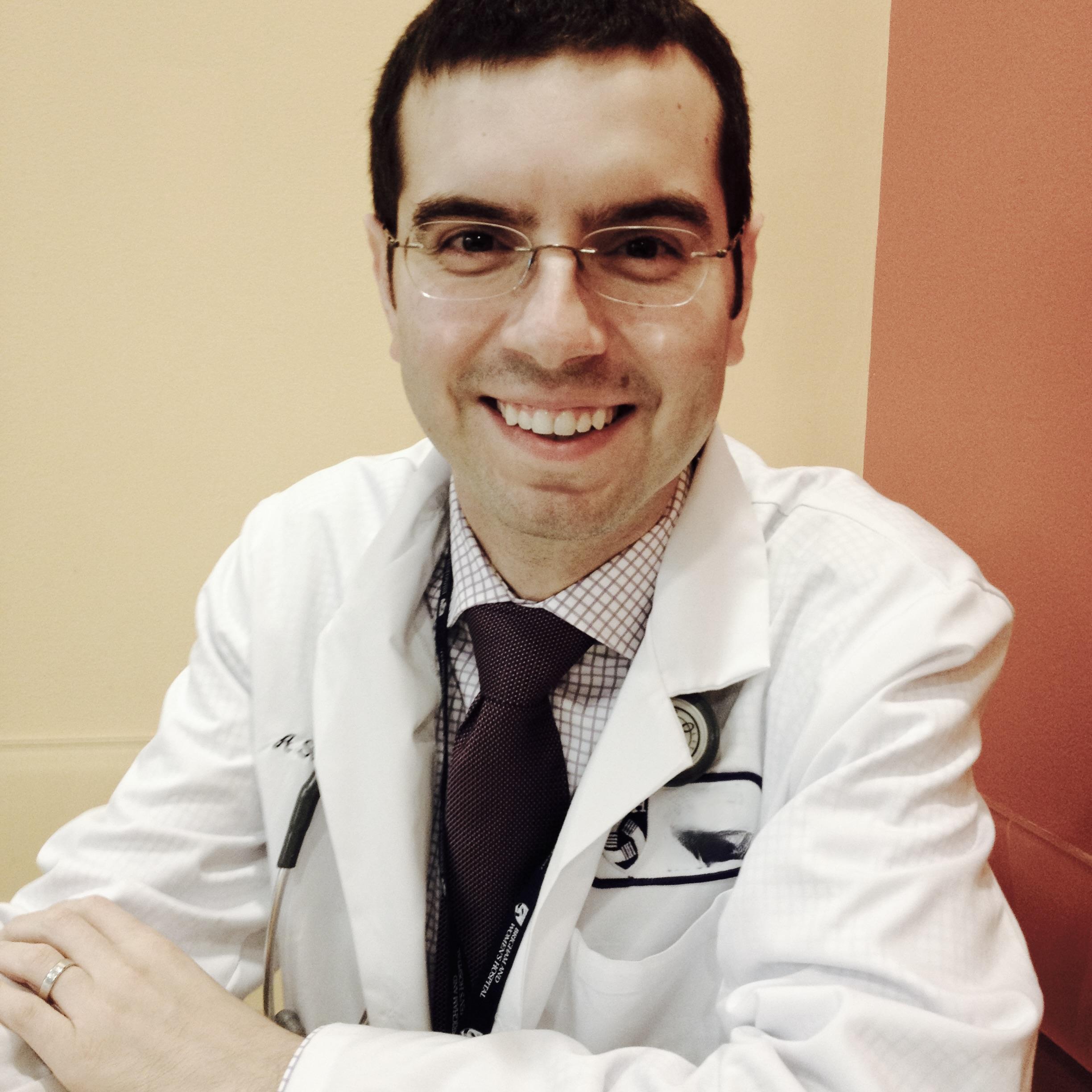A man in a white doctor coat and stethoscope smiling.