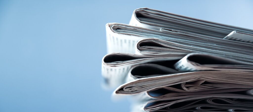 A photograph of a stack of newspapers in front of a blue background.